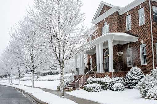 A traditional, brick home during a Winter snow storm. The architecture reflects old styles, however, the construction of the homes has used modern materials and finishes. Nice image for any Winter project.