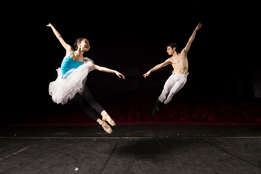 Two ballet dancers jumping high, in air. At theater on a stage.