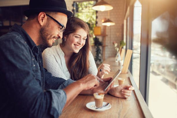 Happy couple in a coffee shop using digital tablet Happy couple in a coffee shop surfing internet on digital tablet. Young man and woman in a restaurant looking at touch screen computer. cafe tablet stock pictures, royalty-free photos & images