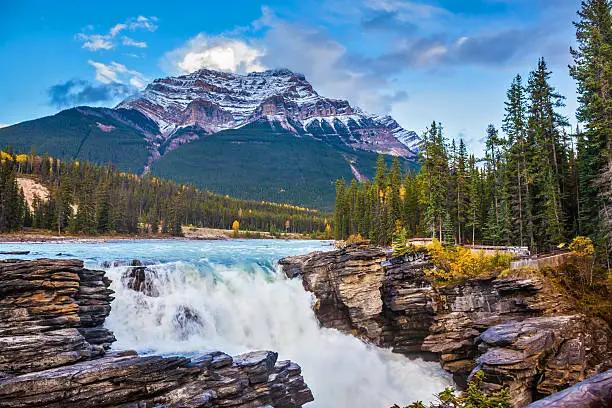 Powerful picturesque waterfall Athabasca. Pyramidal mountain covered with the first snow. Canada, Jasper National Park
