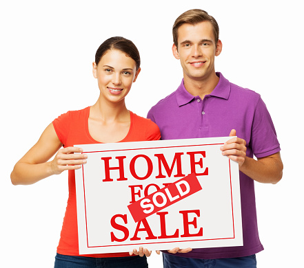 Portrait of confident young couple holding For Sale and Sold sign against white background. Horizontal shot.
