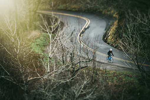 A man cycling in a beautiful Oregon state forest setting on the Historic Columbia River Highway.  He has a bright blue street bike that stands out from the green of the surrounding trees.