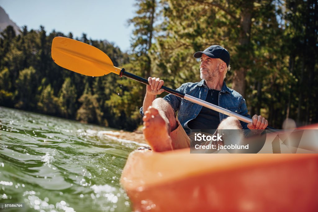 Mature man paddling a kayak Portrait of a mature man with kayak in a lake. Caucasian man paddling a kayak on summer day. Men Stock Photo