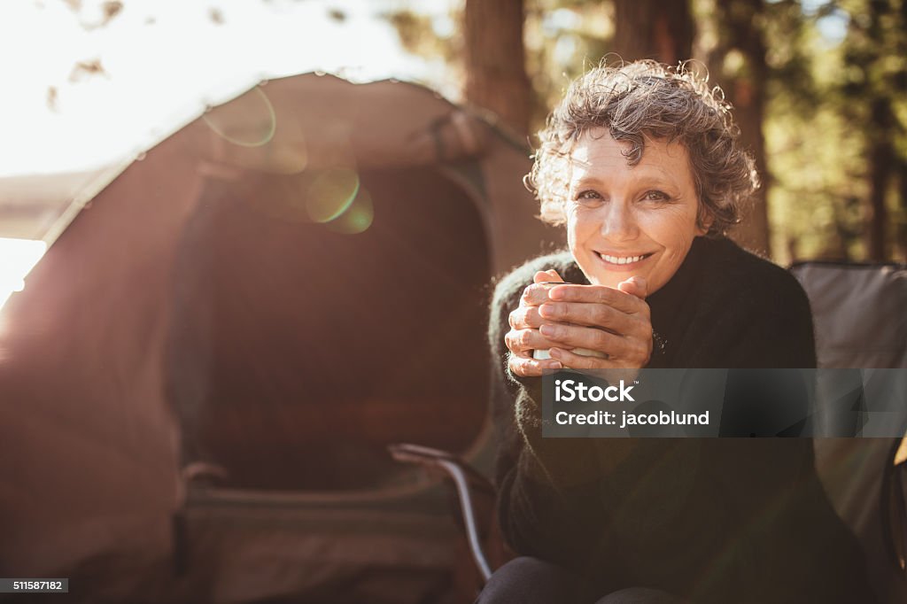 Smiling mature couple on camping Portrait of a happy mature woman holding coffee cup while sitting in front of a tent and looking at camera. Senior caucasian woman having tea at campsite on a sunny day. Mature Women Stock Photo