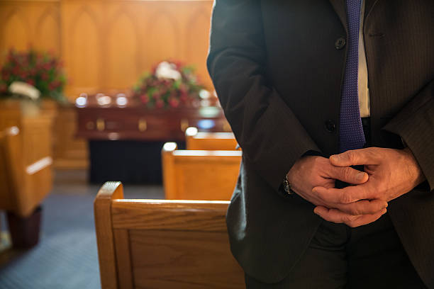 Funeral Man stands wearing a suit with his hands clasped inside a chapel before a funeral service chapel stock pictures, royalty-free photos & images