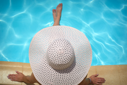 beautiful woman in a white hat sitting on the edge of the pool.