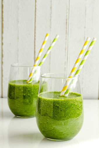 Two glasses filled with spinach and kale green detox smoothie with yellow and green swirled straws