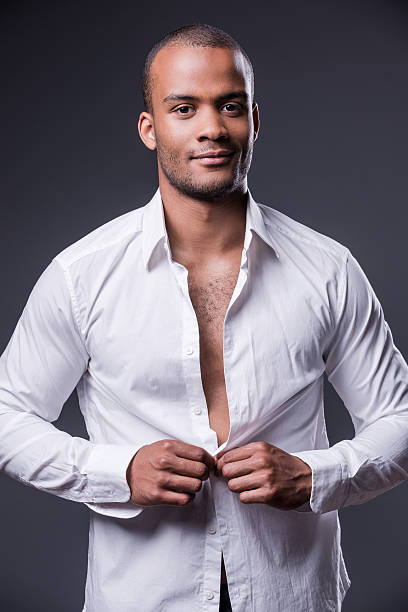 It is my favorite shirt. Handsome young black man dressing up his shirt and smiling while standing against grey background buttoning stock pictures, royalty-free photos & images