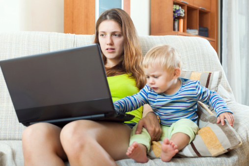 Whiner woman with a crying baby, working on the Internet with a laptop in the house