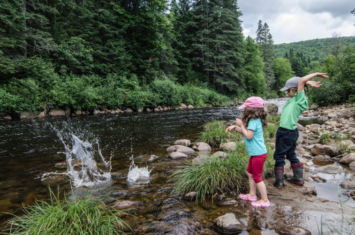 Two kids throwing rocks in the river to make splashes