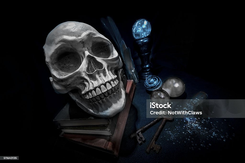 Skull on books and magic crystal balls with rusty keys Human skull on books in a pool of light. Crystal balls glowing and cloudy. Spilled glass jar and two rusty old keys. Weird wide angle and Dutch angle for spooky effect. Afterlife Stock Photo