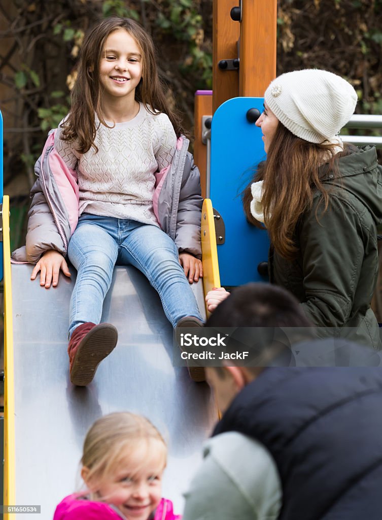 parents with two daughters playing at children's slide Excited parents with two daughters playing at children's slide Activity Stock Photo