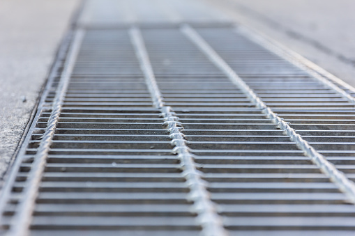 Black and white close up of a sidewalk subway grate with shallow depth of field.