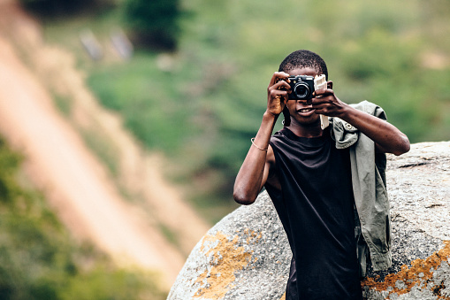 Young african man with camera hiking out in the nature.