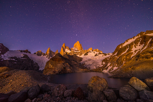 The iconic Mt. Fitz Roy & the beautiful blue Laguna de los Tres under a starry night sky in the Patagonia region of Argentina.