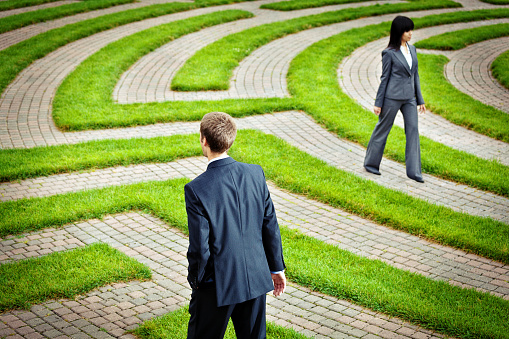 A business man and business woman, two people, Caucasian and Asian, wandering in the corporate maze searching for a way to their occupation, job, and career future, or contemplating their company financial future and seeking solutions. Concept of business problem solving and management strategy.
