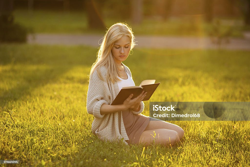 Girl sitting on the grass and reading a book Blonde girl sitting on the grass and reading a book Adult Stock Photo