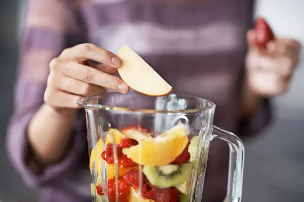 A closeup cropped shot of a woman's hand putting sliced fruits into a blender