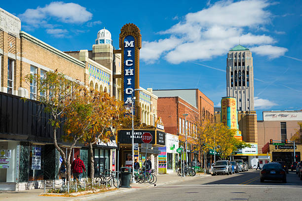 Liberty Street Scene in Ann Arbor Ann Arbor, United States - October 18, 2015: People walking in the sidewalk of Liberty Street in Downtown Ann Arbor, with storefronts and the Michigan Theater sign, State Theater sign, cars and parked bicycles in the scene, and the Burton Memorial Tower in the distance, during a day with a blue sky with clouds. michigan stock pictures, royalty-free photos & images