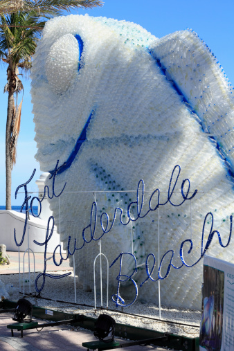 Fort Lauderdale, Florida, USA - February 3, 2013: Large plastic bottles fish sculpture seen closeup with a Fort Lauderdale Beach sign in front of it on the beach.
