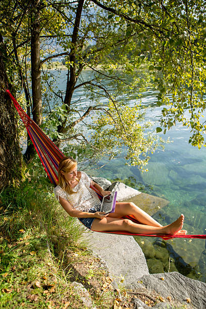 istock Young woman on hammock relaxing by river with digital tablet. 511668819