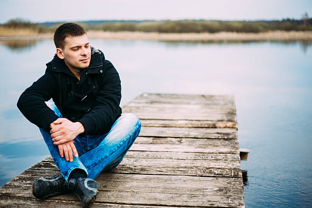 istock Young handsome man sitting on wooden pier, relaxing,  thinking, 511713913