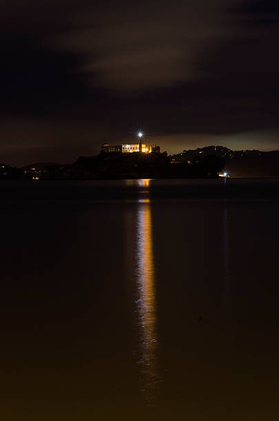 Alcatraz island, San Francisco, California The Alcatraz Penitentiary island, now a museum, in San Francisco, California, United States of America. A night view of light reflected in the sea from the lighthouse, prison buildings and the San Francisco Bay. lighthouse lighting equipment reflection rock stock pictures, royalty-free photos & images