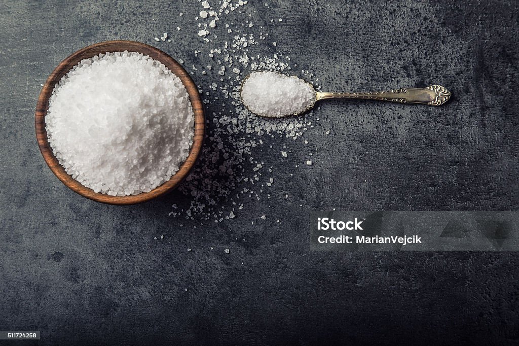 Salt. Coarse grained sea salt on granite background Salt. Coarse grained sea salt on granite - concrete  stone background with vintage spoon and wooden bowl. Salt - Mineral Stock Photo