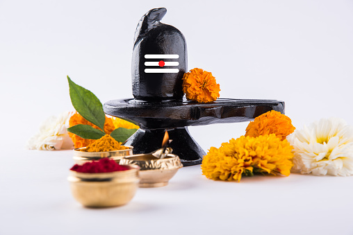Shiva Linga made up of black stone decorated with flowers & bael leaf known as Aegle marmelos, over orange background, maha shiva ratri a festival of hindu God shankar or shankar bhagwan or bholenath