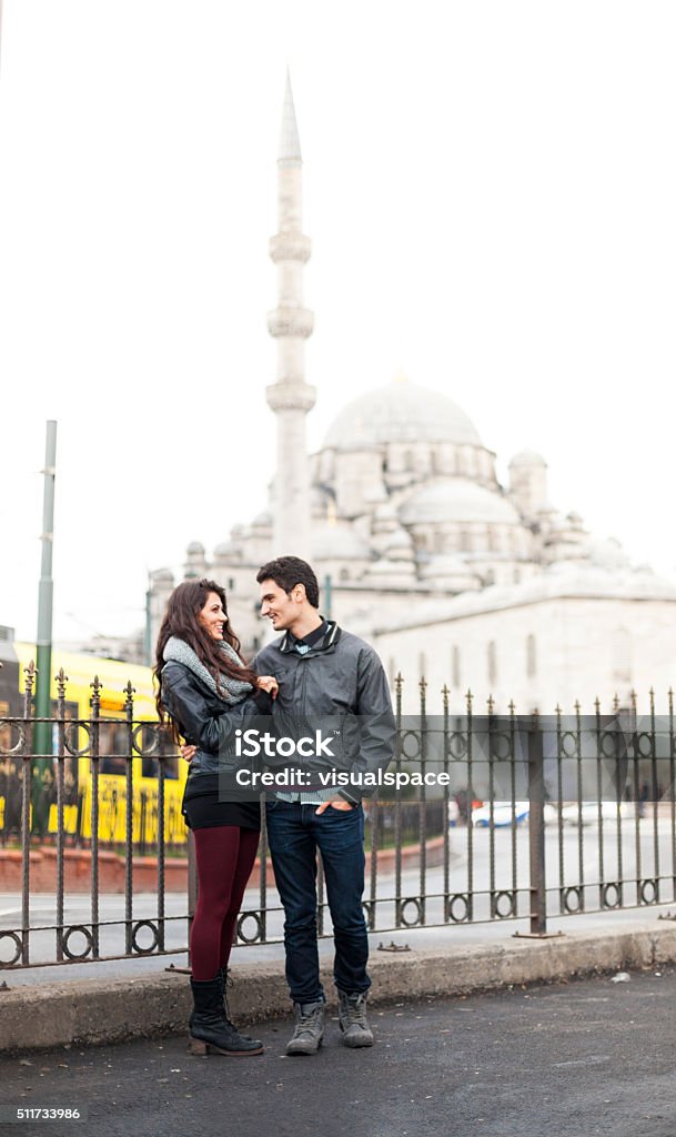 Young Couple Next To a Mosque in Istanbul Young turkish couple is standing close to each other next to a metal fence surrounding a roundabout next to the Blue Mosque. The couple looks positive, cute and carefree, wears fashionably youth clothing. A yellow public transport facility is passing by in the background. Image contains copy space. Made in Istanbul, Turkey. 20-29 Years Stock Photo