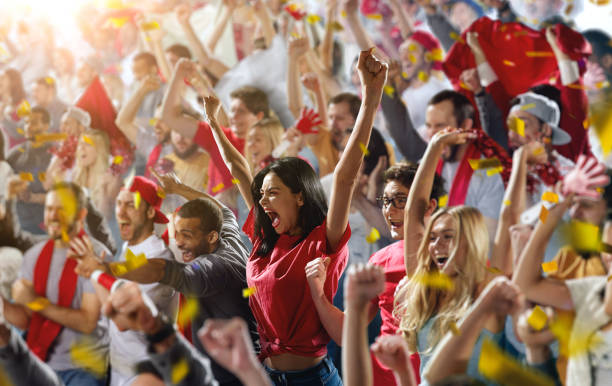 Sport fans On the foreground a group of cheering fans watch a sport championship on stadium. One girl stands with his hands up to the sky. People are dressed in casual cloth. supporter stock pictures, royalty-free photos & images