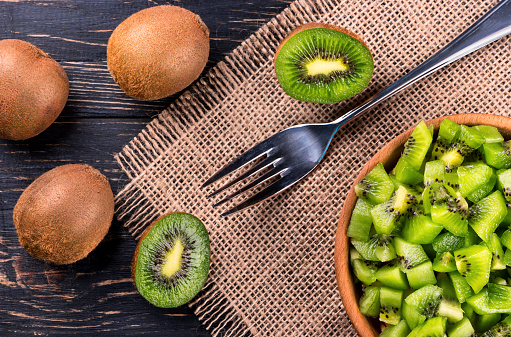 Wooden bowl with a salad of kiwi fruit and a fork on the table top view