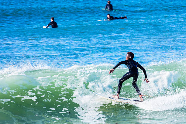 African teenager surfing  in Kommetjie beach Cape Town, South Africa - November, 9th 2015: An African teenager surfing a wave in Kommetjie beach, all confident and in balance. This beach is well frequented by surfing enthusiasts in Cape Town. Other surfers in the background. kommetjie stock pictures, royalty-free photos & images