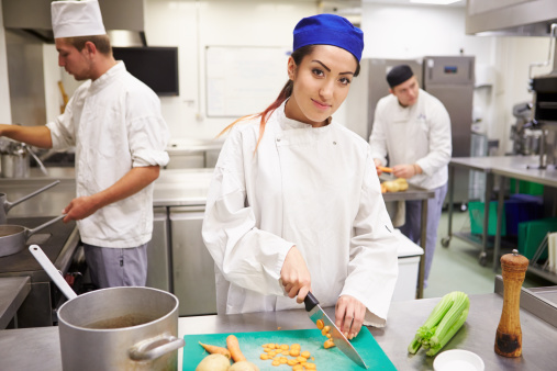 Students Training To Work In Catering Industry Chopping Vegetables. Looking To Camera