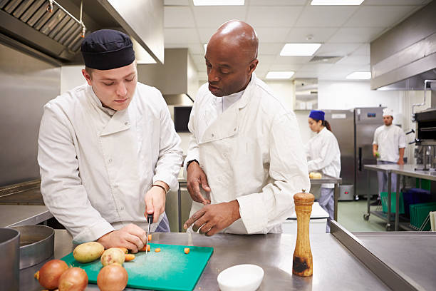 enseignant aidant les étudiants formation de travailler dans le service traiteur - chef restaurant cooking african descent photos et images de collection