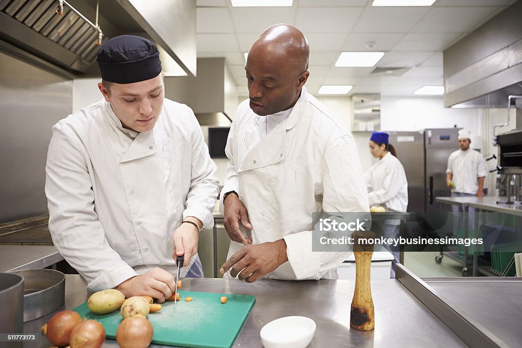 Teacher Helping Students Training To Work In Catering Teacher Helping Students Training To Work In Catering Chopping Vegetables Trainee Stock Photo