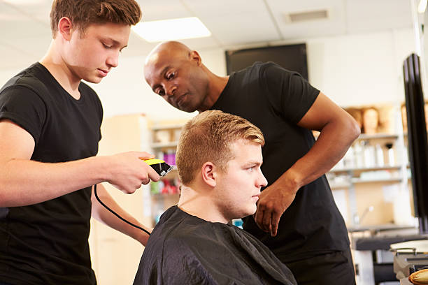 Teacher Helping Students Training To Become Hairdressers Teacher Helping Male Students Training To Become Hairdressers teenager boy haircuts stock pictures, royalty-free photos & images