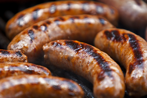 A group of Italian Sausages cook on a grill.