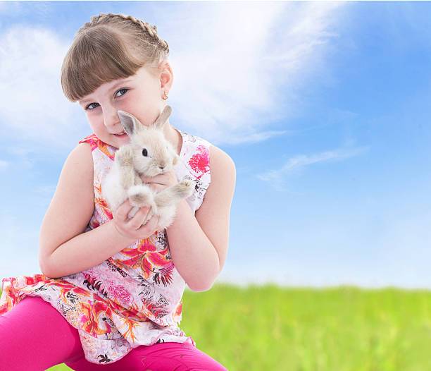 istock Little girl holding a rabbit sitting on meadow. 511777771