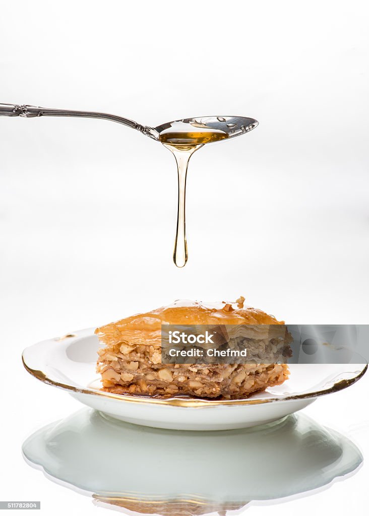 Honey dripping from sterling silver spoon onto baklava Isolated in white background. Antique English fine bone china plate. Afternoon tea time. Antique sterling silver spoon. Baklava Stock Photo