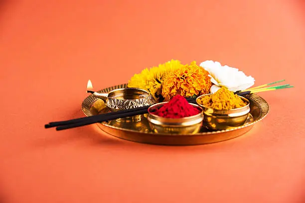 Beautifully Decorated Pooja Thali for diwali celebration to worship, huldi or turmeric powder and kumkum, flowers, scented sticks in brass plate on orange background, hindu puja thali