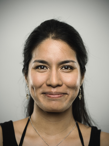 Studio portrait of a mixed race young woman looking at camera with happy expression. The woman has around 30 years and has long hair and wears earrings and a necklace. Vertical color image from a medium format digital camera. Sharp focus on eyes.