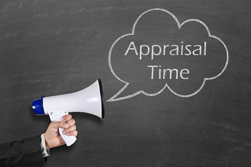 Cropped image of a businessman's hand holding a megaphone against text Appraisal Time in speech bubble on blackboard. Performance appraisal is a part of career development. Performance appraisals are regular reviews of employee performance with in organizations.