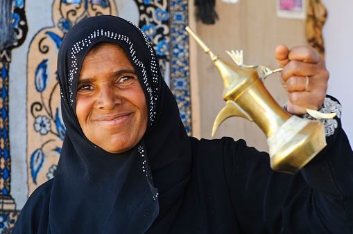 Petra, Jordan - November 12, 2010: A Bedouin woman in her mid-thirties holding up a traditional Bedouin coffee pot made of brass or copper. 