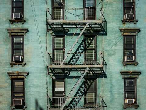 View of a fire escape and its shadow on the side of a green brick New York apartment