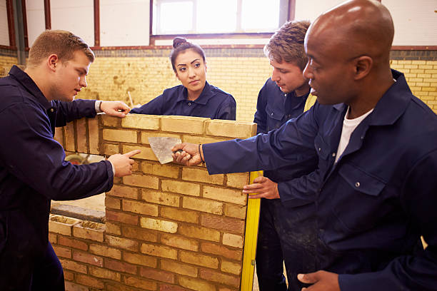 Teacher Helping Students Training To Be Builders Teacher Helping Students Training To Be Builders Standing Next To Brick Wall bricklayer stock pictures, royalty-free photos & images