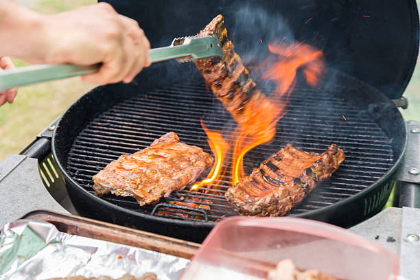 A man uses tongs to turn over ribons on a grill