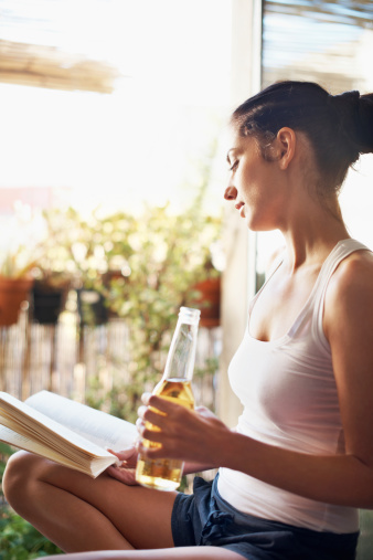 Shot of an attractive young woman having a beer while reading a book