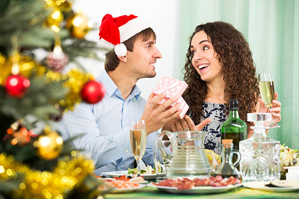 Man giving present to woman Attractive young man giving present to woman during Christmas dinner in home wonderingly stock pictures, royalty-free photos & images