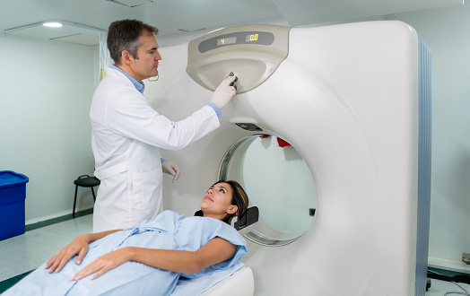Doctor at the hospital doing a CAT scan on a young woman lying down in a hospital gown - radiology concepts